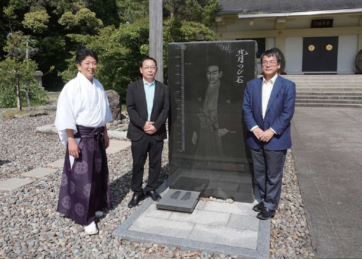 福井県護国神社の名物「背のび石」を囲む海堂さん、角鹿尚計さん（中央）、宮川貴文さん（左）。後方にあるのが「急流中底之柱」